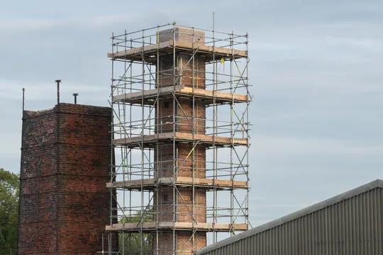Scaffolding staged around a tall brick chimney so masons can work at height